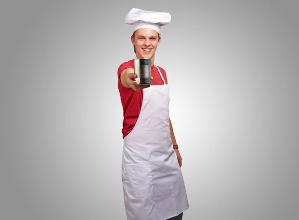 Portrait of young cook man holding a metal tin can over grey bac — Stock Photo, Image