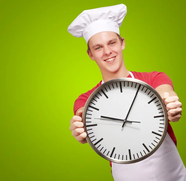 Portret młodej gotować człowieka posiadającego zegar na zielonym tle — Zdjęcie stockowe