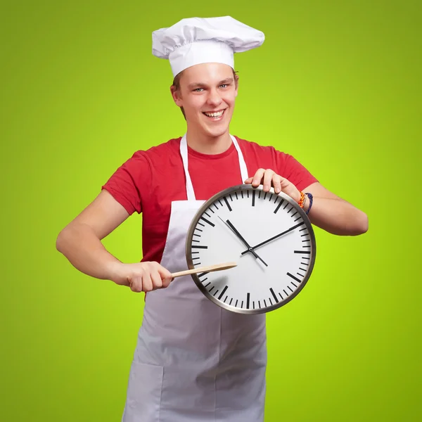 Portret młodej gotować człowieka wskazując zegar nad zielonym deseń — Zdjęcie stockowe