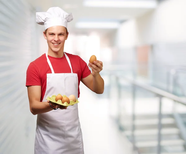Portrait of young cook man holding egg box at entrance of buildi — Stock Photo, Image