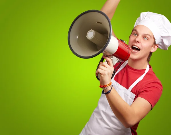 Portrait of young cook man shouting with megaphone over green ba — Stock Photo, Image