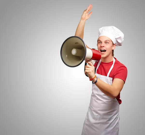 Портрет молодого повара, кричащего с мегафоном над серым баком — стоковое фото