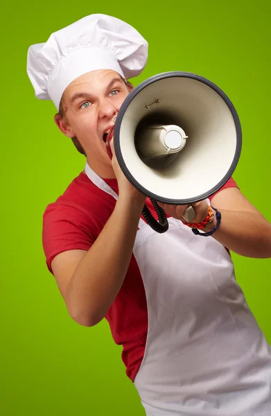 Retrato del joven cocinero gritando con megáfono sobre verde b — Foto de Stock