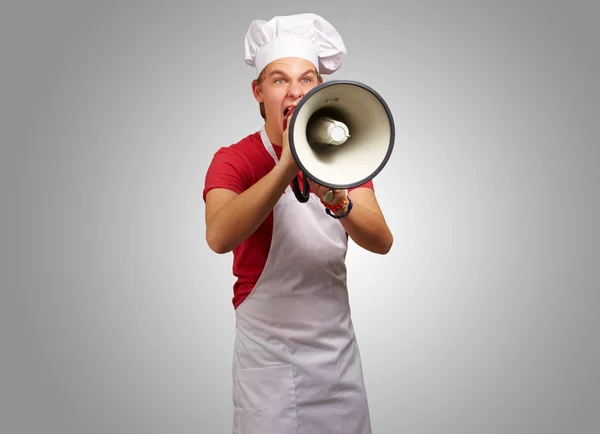 Portret van jonge kok man schreeuwen met megafoon over grijs ba — Stockfoto