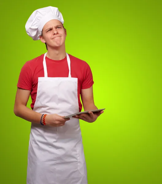 Retrato del joven cocinero sosteniendo una tableta digital y pensando — Foto de Stock