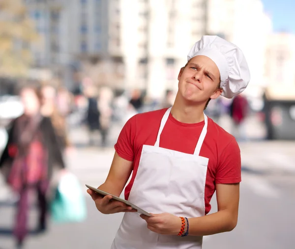 Portrét mladého kuchaře muž držící digitální tabletu a myšlení — Stock fotografie