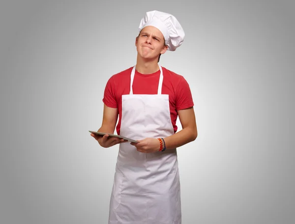 Portrait d'un jeune cuisinier tenant une tablette numérique et réfléchissant — Photo