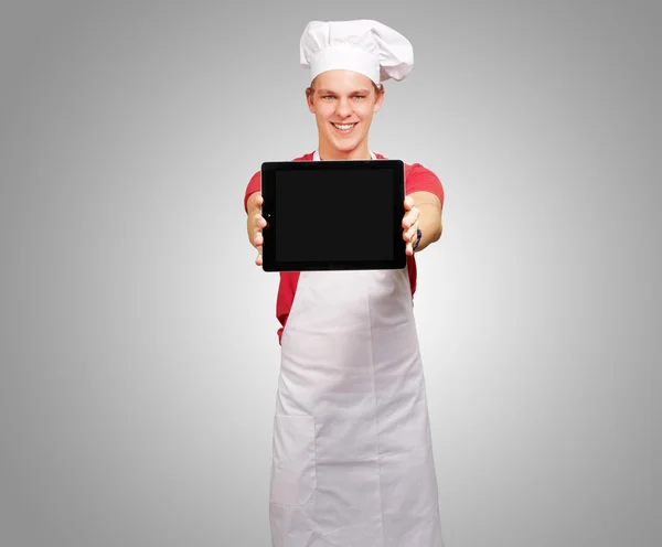 Retrato de jovem cozinheiro mostrando um tablet digital sobre ba cinza — Fotografia de Stock