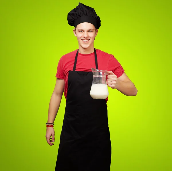 Портрет молодого повара, держащего молочную банку над зеленой спинкой — стоковое фото