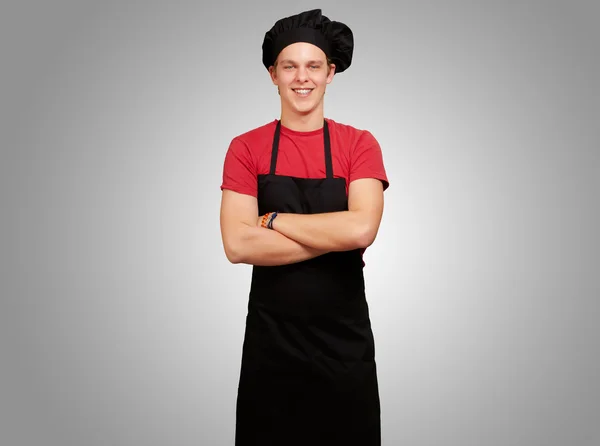 Portret młodej gotować człowieka noszenie munduru i uśmiechając się przez szare — Zdjęcie stockowe
