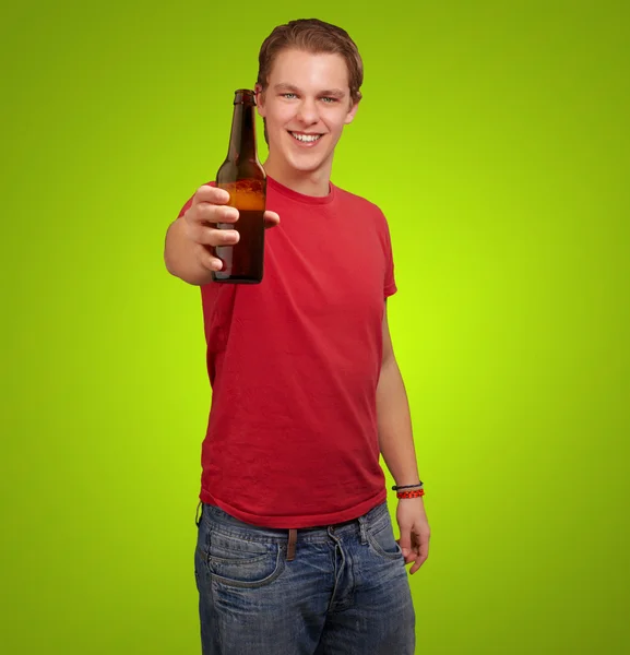 Portrait of young man holding beer over green background — Stock Photo, Image