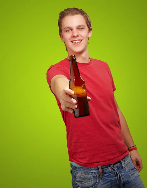 Portrait of young man holding beer against a green background — Stock Photo, Image