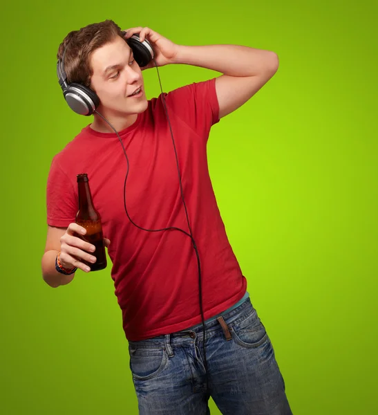 Portrait of young man listening music and holding beer on green — Stock Photo, Image