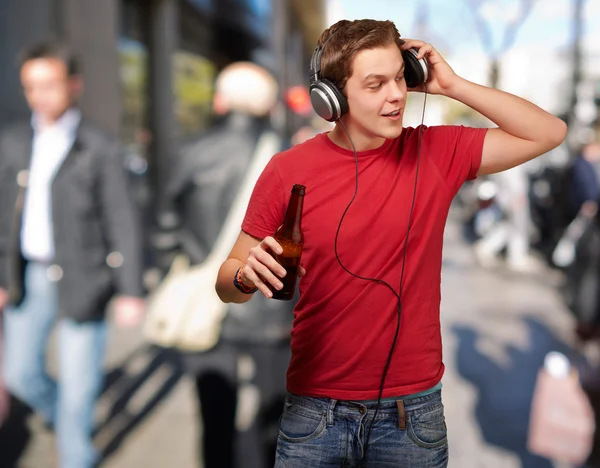 Portrait of young man listening music and holding beer at street — Stock Photo, Image