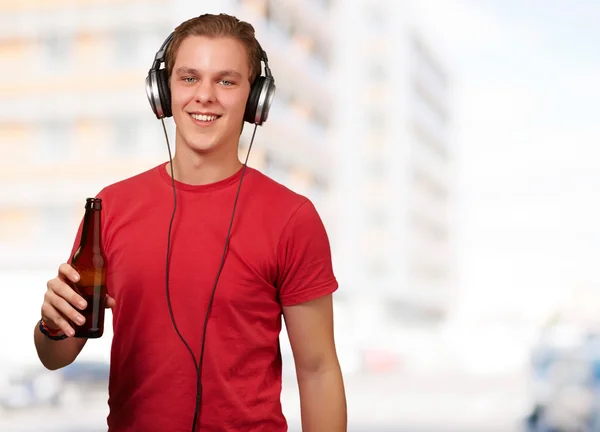 Retrato de jovem ouvindo música e segurando cerveja contra um — Fotografia de Stock