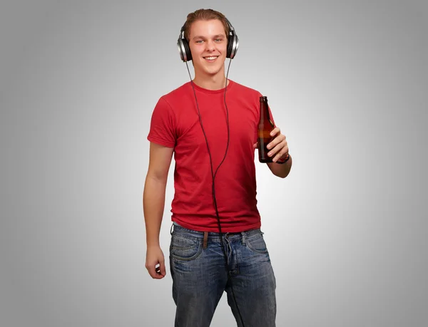 Retrato do jovem ouvindo música e segurando cerveja sobre cinza — Fotografia de Stock