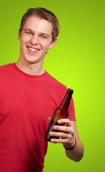 Junger Mann hält Bier über grünem Hintergrund — Stockfoto