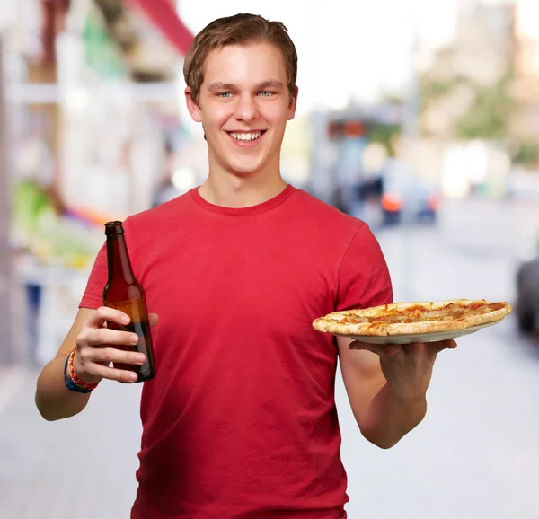 Porträtt av ung man håller pizza och öl på street — Stockfoto
