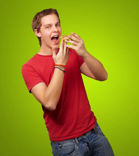 Portrait of young man eating pizza over green background — Stock Photo, Image