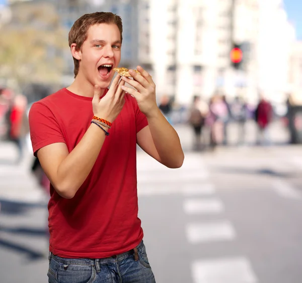 Porträt eines jungen Mannes, der an einer belebten Straße Pizza isst — Stockfoto