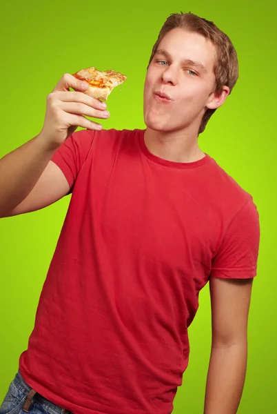 Portret młody człowiek jedzenie pizzy część nad backgorund zielony — Zdjęcie stockowe