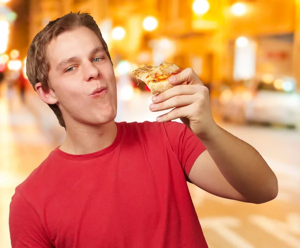 Portrait of young man eating pizza portion at night city — Stock Photo, Image