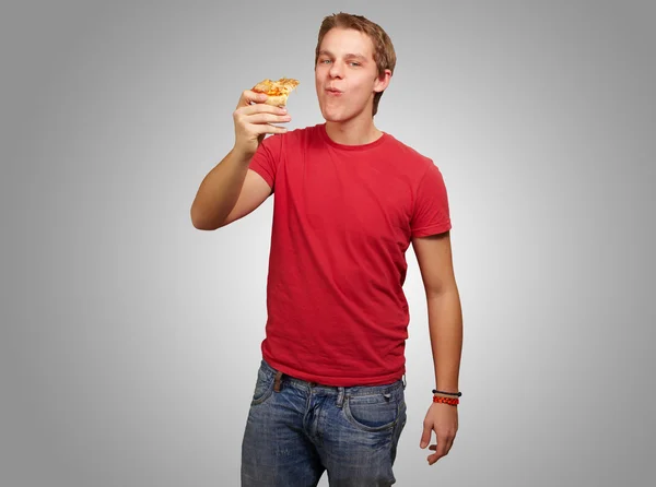 Portrait of young man eating pizza portion over grey backgorund — Stock Photo, Image
