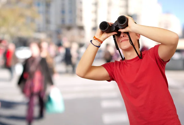 Portrait of young man with binoculars at crowded street — Stock Photo, Image