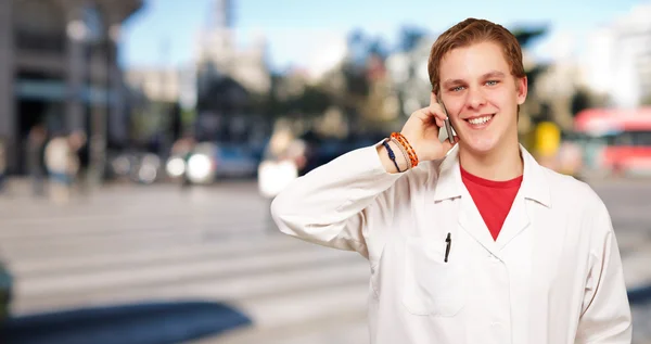 Portrait of young academic talking on mobile at crowded street — Stock Photo, Image