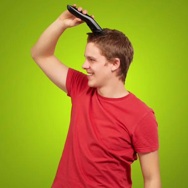 Porträt eines jungen Mannes, der seine Haare über grünem Hintergrund schneidet — Stockfoto