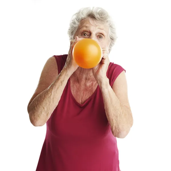 Starší žena fouká balónek — Stock fotografie