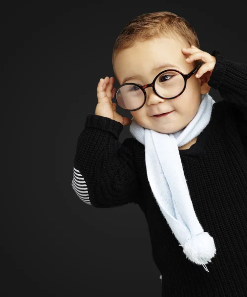 Retrato de niño divertido sosteniendo sus gafas contra un respaldo negro — Foto de Stock
