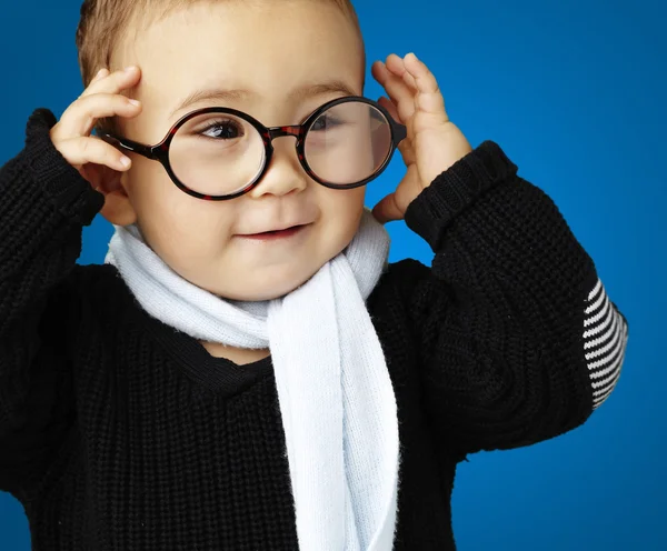 Ritratto di bambino divertente che tiene gli occhiali contro un dorso blu — Foto Stock
