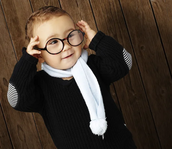 Portrét legrační dítě drží své brýle dřevěné stěny — Stock fotografie