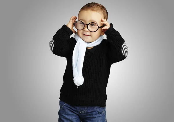 Retrato de niño divertido sosteniendo sus gafas contra un fondo gris — Foto de Stock