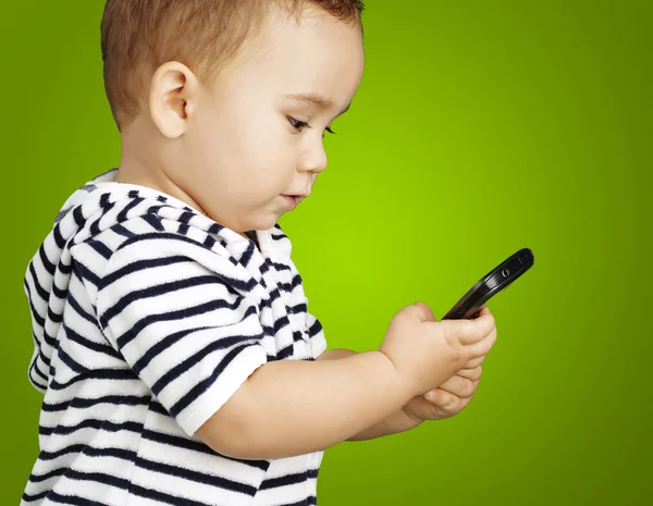 Porträt eines lustigen Kindes, das sein Handy vor grünem Hintergrund berührt — Stockfoto