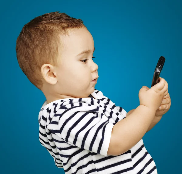 Porträt eines lustigen Kindes, das sein Handy auf blauem Hintergrund berührt — Stockfoto