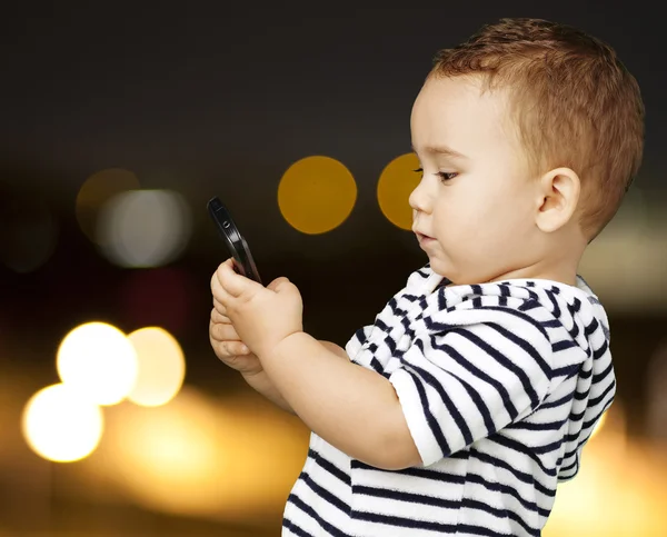 Retrato de niño divertido tocando móvil en la ciudad por la noche — Foto de Stock