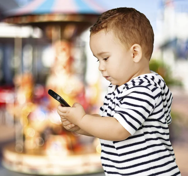 Portrait of funny kid touching mobile against a carousel — Stock Photo, Image