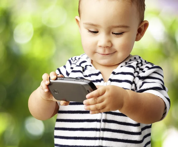 Портрет забавного ребенка, играющего с мобильником в парке — стоковое фото