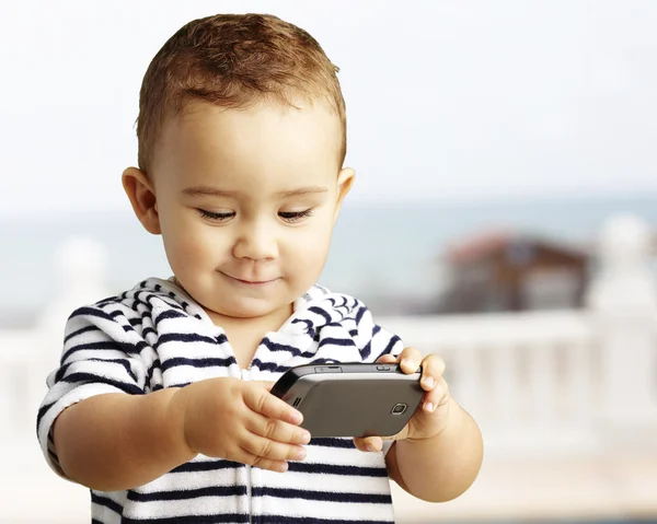 Porträt eines lustigen Kindes, das in Strandnähe mit dem Handy spielt — Stockfoto