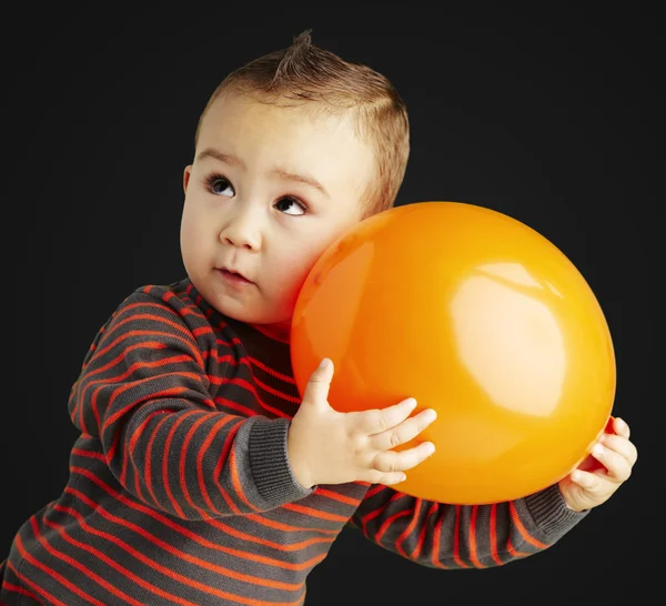 Portrait of funny kid holding a big orange balloon over black ba — Stock Photo, Image