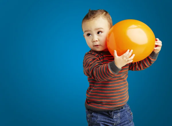 Portrait of funny kid holding a big orange balloon over blue bac — Stock Photo, Image