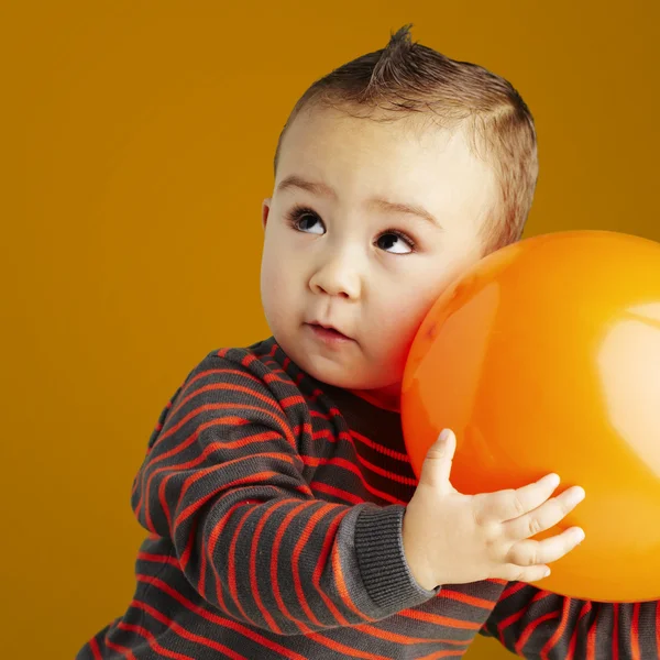 Retrato de un niño divertido sosteniendo un gran globo naranja sobre naranja b — Foto de Stock