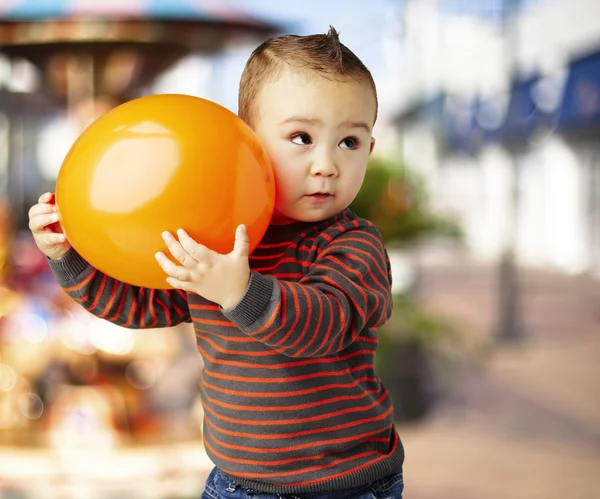 Portrait of funny kid holding a big orange balloon against a car — Stock Photo, Image