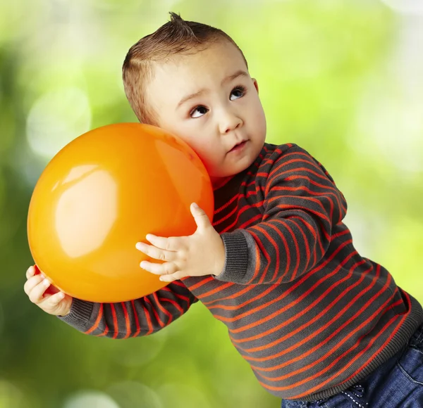 Portrait of funny kid holding a big orange balloon at park — Stock Photo, Image