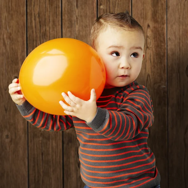 Portrait of funny kid holding a big orange balloon against a woo — Stock Photo, Image