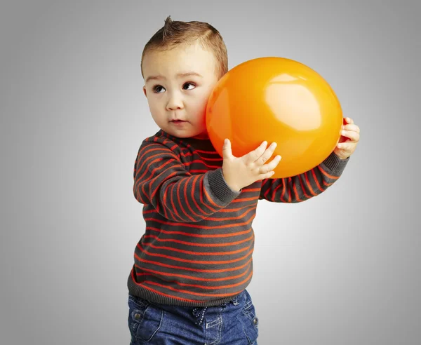 Portrait of funny kid holding a big orange balloon over grey bac — Stock Photo, Image