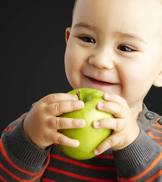 Портрет смешного ребенка, держащего зеленое яблоко и улыбающегося над черным — стоковое фото