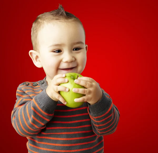 Portrait of funny kid holding green apple and smiling over red b — Stock Photo, Image